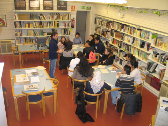 11 alumnes d'ESO entre nois i noies, juntament amb la seva professora, es troben asseguts al voltant de dues taules mentre escolten les explicacions de l'arxiver del Districte de Sant Martí amb l'objectiu de realitzar-hi una activitat.